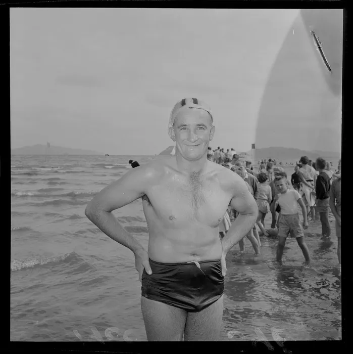 An unidentified man who just completed the Somes Island Petone swim on Petone Beach with children looking on, Wellington City