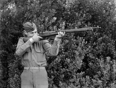 [U.S. military serviceman poses looking down the barrel of a rifle]