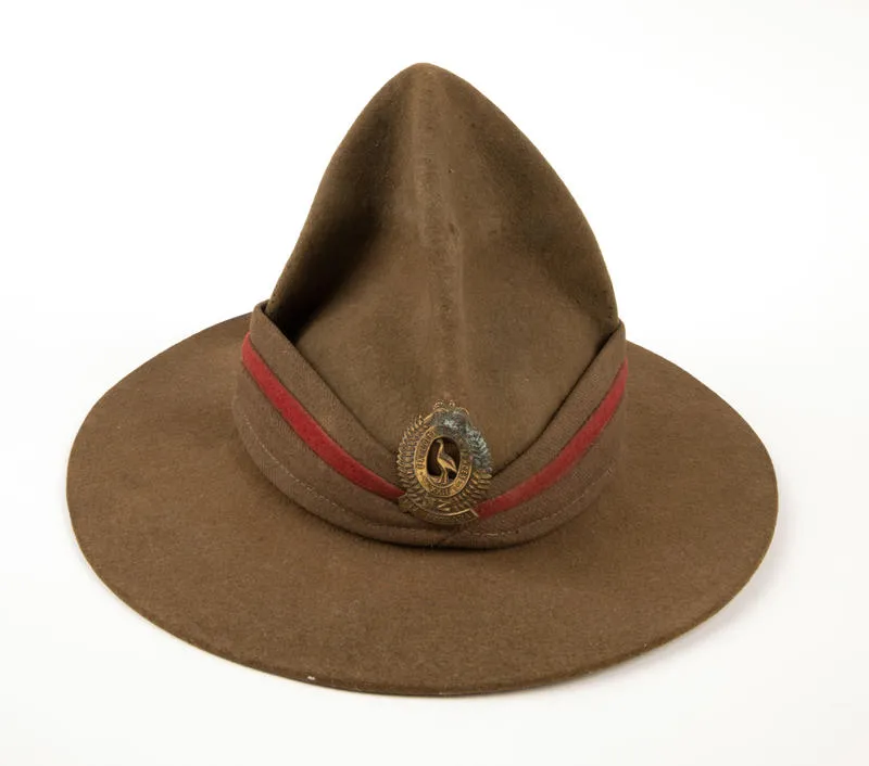 Lemon Squeezer Hat. - A brown serge lemon squeezer hat as part of the uniform for the Expedition Forces. Lemon Squeezer hat, as a part of the Expedition Forces uniform.  Made from brown woollen felt, this item is adorned with a brown and red serge puggaree.  It's hat badge depicts a set of fern fronds either side, with a Moa in the centre, and a crown at the top.The ...