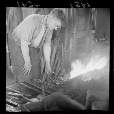 Image: Unidentified blacksmith heating metal object in a forge at a workshop, Johnsonville, Wellington