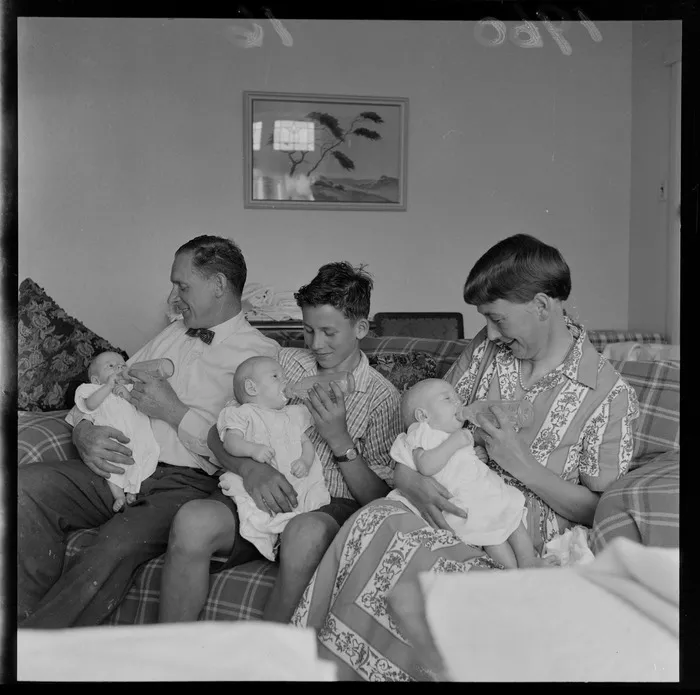 Fullerton triplets being bottle fed by their parent and older brother on the sofa at home in Lower Hutt