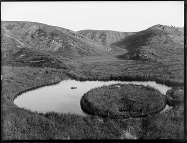 Image: A lake with a circular floating island, including two men in a dinghy, Whakaki, Wairoa District
