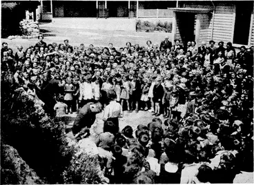 Image: isvening -Post" Pboto. Children assembled in the playground at Island Bay School yesterday whilst one of their number, seen on the left, presented a gift to the headmaster, Mr. O. J. Howarth, who is leaving the school to take over the headmaster ship of Tail" marunui District High School. (Evening Post, 17 December 1938)