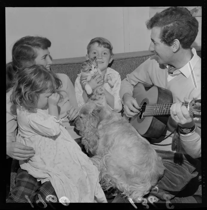 Folk musician, theologian and writer Peter Cape with guitar and family within their home at an unknown location, probably Wellington Region