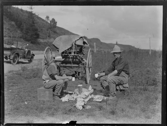 Unidentified drovers drinking tea and eating bread during smoko break on rural roadside, including car [Leo White's Austin 7?] and cart in background, location unknown