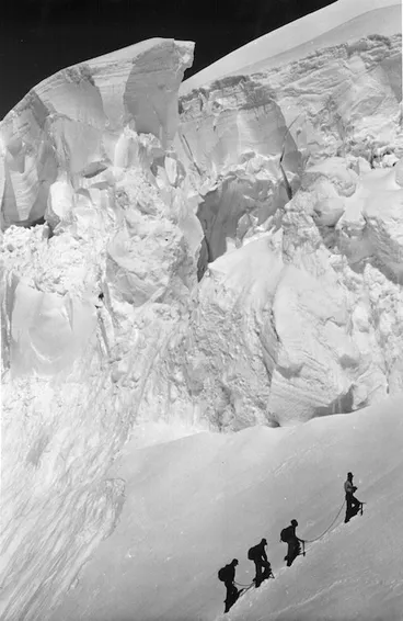 Image: Four mountaineers climbing a snow covered slope beneath ice cliffs