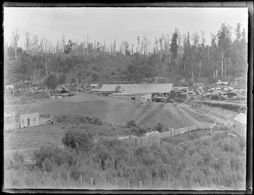 Image: The Kakahi Sawmill with sawdust mound and stacked timber, with forest covered hills beyond, Kakahi Settlement, Manawatu-Whanganui Region