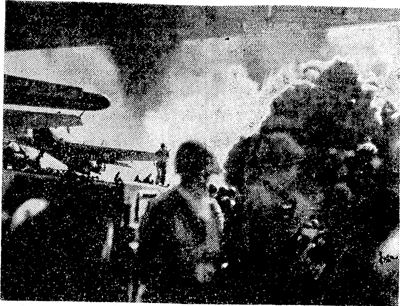Smoke from a Japanese shell, exploding off the port quarter, shrouds the United States escort carrier Kiikun Bay during the second battle of the Philippines. Planes are poised on the carrier's flight deck ready to join in the fray. (Evening Post, 29 January 1945)