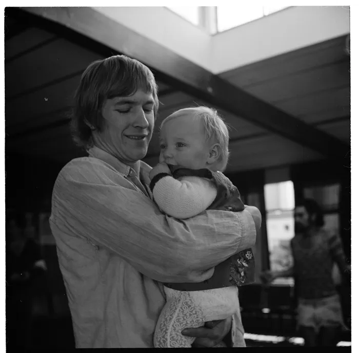 Young woman with a child and a black dog, and, a group outside a corrugated iron building