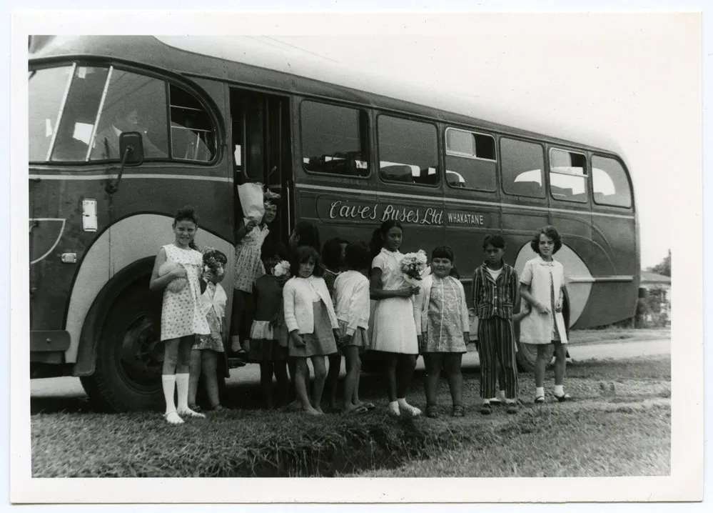 A group of Maori children standing beside a bus
