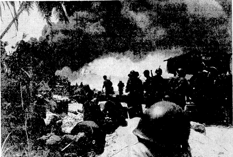 The M^hUrdted States Infantry, formerly known as New York's "Fighting^ 169 th" landing on Makin Island and\f advancing under sharp fire from Japanese snipers. The smoke is coming from a Japanese ■ oil dump which had been hit by navy gunners. (Evening Post, 19 February 1944)