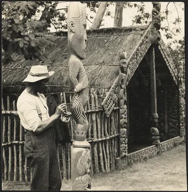 Image: Man painting a moko on a carved wooden figure at the Whakarewarewa model village