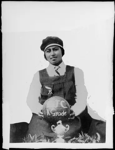 Image: Unidentified champion female netballer holding a ball with SJC A grade written on it, also a small trophy in front with a kiwi on the lid and a badge pinned on her uniform, probably Hastings district