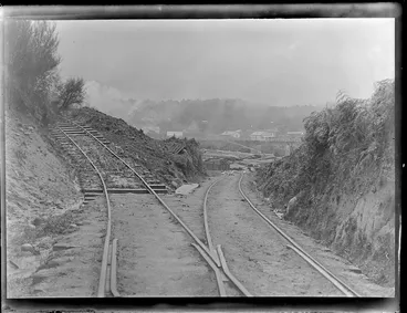 Image: Railway lines which feed Kakahi Sawmill with logs, stacked logs ready for milling, a rail carriage with cut lumber and the settlement of Kakahi beyond, Manawatu- Whanganui Region