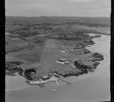 Image: Hobsonville Aerodrome, Auckland, showing a seaplane on the ocean, with five aircrafts on shore on the tarmac next to the hangar