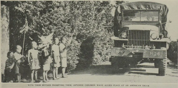 With their mother prompting them, Japanese children wave Allied flags at an American truck