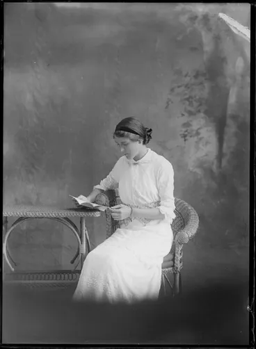 Image: Studio portrait of unidentified woman, wearing a chain bacelet and reading a book, probably Christchurch district