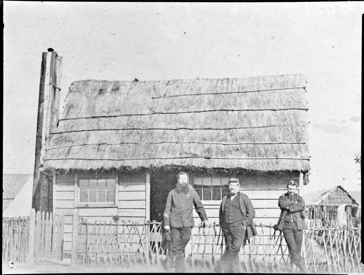 Three men standing in front of a cottage, Ngāruawāhia, 1864