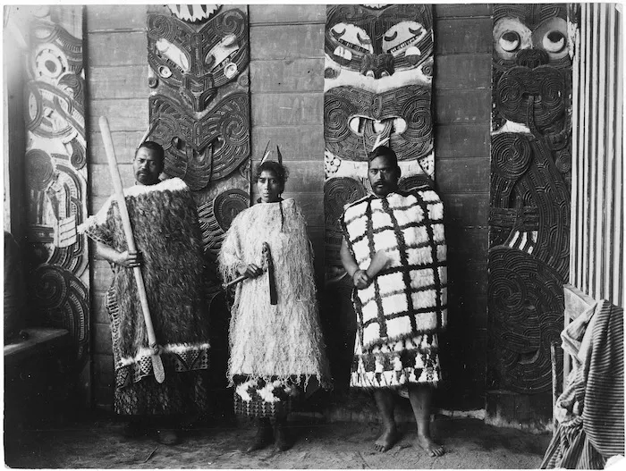 Group on the step of Te Whai-a-te-Motu meeting house at Mataatua standing in front of carved wooden poupou - Photograph taken by W A Neale