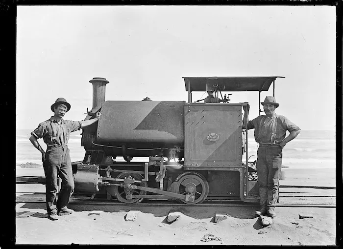 Steam railway locomotive the "Sandfly" with her driver and fireman standing beside, on the Karekare beach tramway.