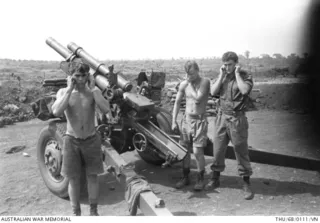 BIEN HOA PROVINCE, VIETNAM. 1968-02. THREE SOLDIERS FROM NEW ZEALAND'S 161ST BATTERY, ROYAL NEW ZEALAND ARMY (RNZA), BLOCK THEIR EARS AS THEIR 105MM HOWITZER GUN FIRES AT ENEMY POSITIONS DURING ..