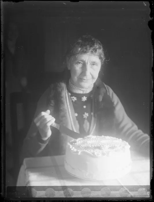 Unidentified woman (possible relative of Lydia and William Williams) cutting a decoratively iced cake, unknown location