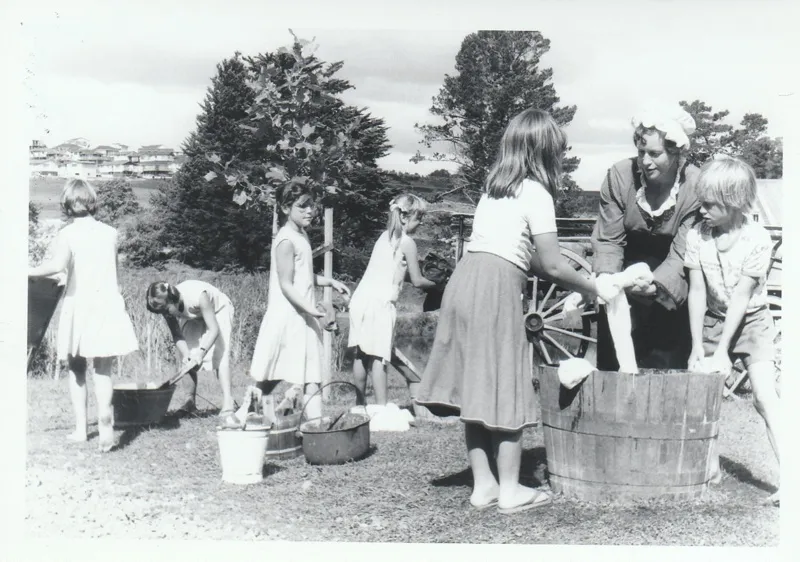 School children learning how to use a mangle in Historical Village during a school visit.