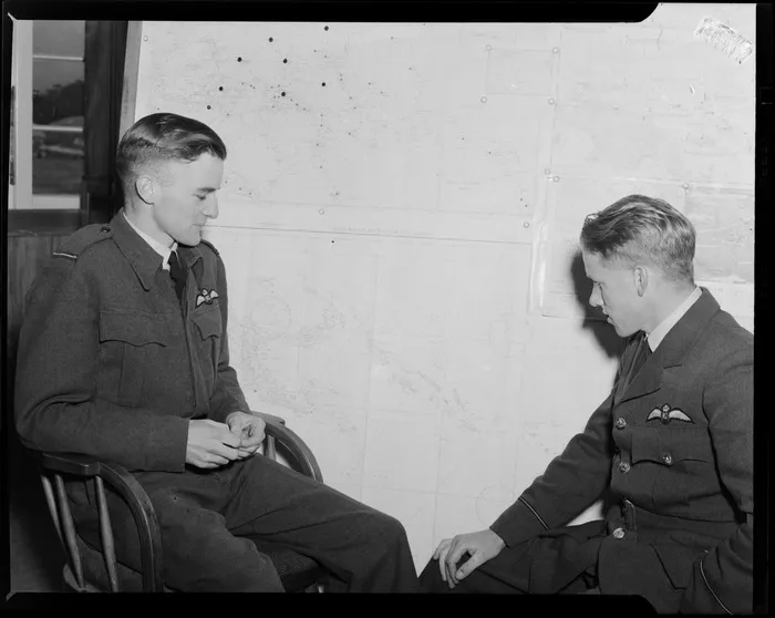 View of the Guadalcanal Operations Room with Flight Sergeant R Lund on left looking at wall maps with an unidentified fellow RNZAF Officer, location unknown