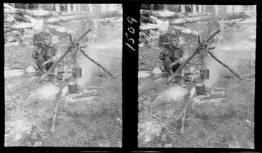 Image: Unidentified man by campfire reading a book, with wooden tripod holding up pot over fire, location unknown