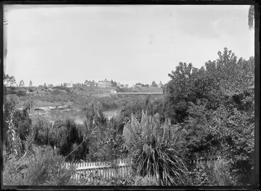 Image: View of Hamilton, Waikato Region, from the garden at Mrs Gwynne's Cottage, including the first traffic bridge, the Waikato River, and from left, St Andrew's Presbyterian Church and Le Quesne's Hotel (3 storey building), and the adjoining Hamilton Hall