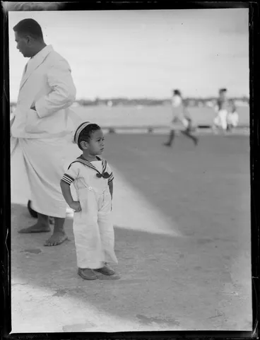 Image: A close-up portrait of local Tongan child in a sailors outfit and unidentified man behind, Tonga