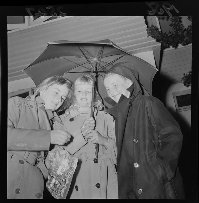 Three unidentified Hutt Valley girls under an umbrella on Guy Fawkes, including a sparkler and bag of fireworks