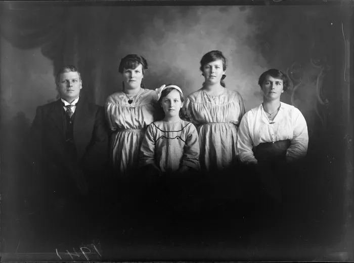 Studio portrait of unidentified family with their two young adult daughters in matching embroidered dresses and younger daughter with hair bow, Christchurch