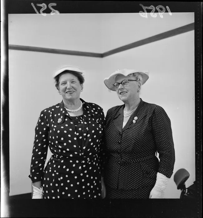 Esther Parsonage and C McKay who are both dressed up in two-piece outfits that include hats, glasses, pearls, brooches and gloves