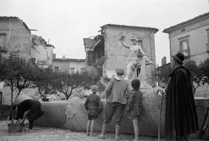 People looking at an undamaged statue, among the ruins of Gessopalena, Italy