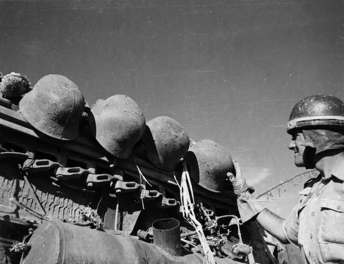 F C Revell inspecting German helmets on a tank near Rimini, Italy, during World War II