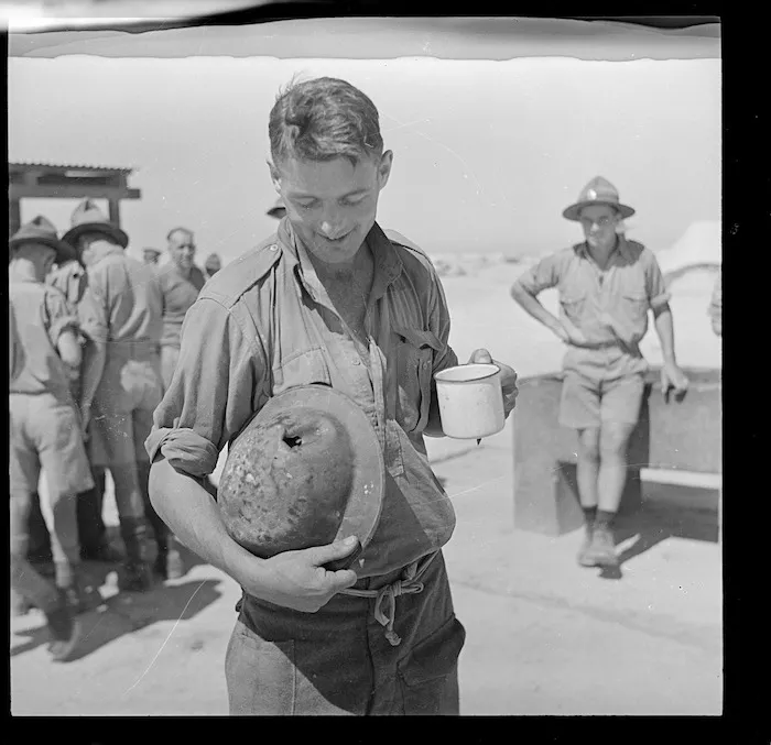 New Zealand soldier in Egypt, after the evacuation from Crete, holding a battered helmet