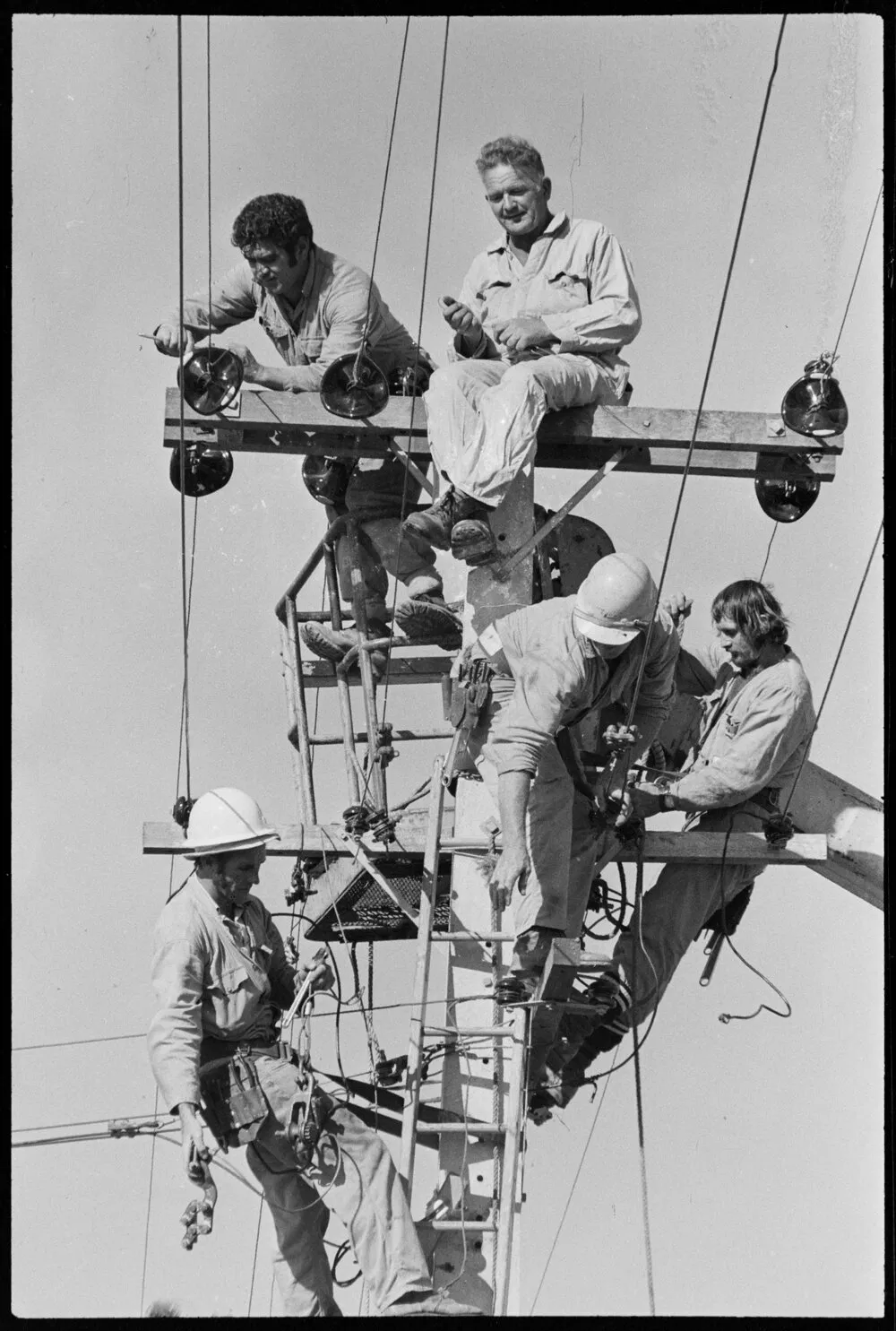 Tauranga Electric Power Board linemen - Linemen from Tauranga Electric Power Board connecting lines to the pole near Cooney's Drive. Top, E. Ormsby (left) and O. Norris, lower, L. Rae, R. Grice and T. Clausen (partly obscured). Published 21 April 1972.