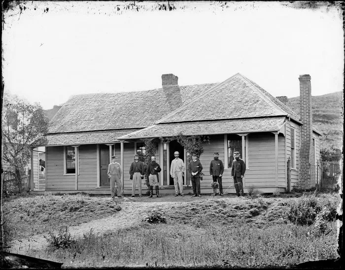 Men standing outside cottage, Whanganui