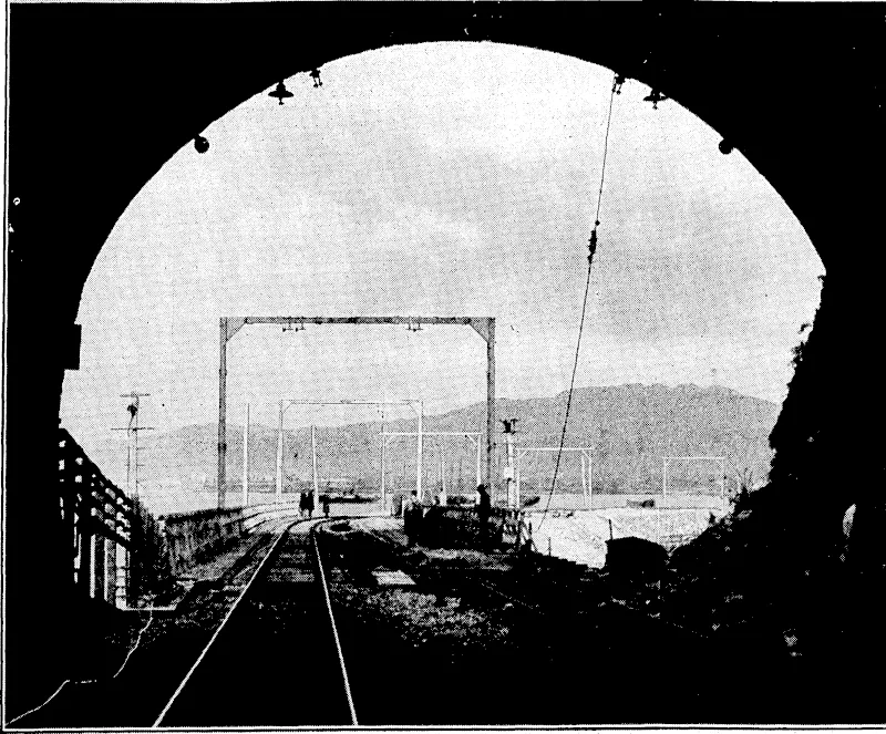 Kvtnnii; ■ l'l'.sf , I'lmlu; ELECTRIFYING THE TAWA FLAT. DEVIATION.—A, view,from the city, portal: of No. 1 tunnel on the Tawa Flat Deviation, show• ing the steel supports for the overhead iviresto be used in connection ' with .the electrification of the line. ' (Evening Post, 15 July 1935)
